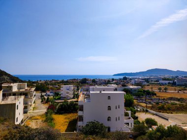 Zarif beyaz binaların ve berrak mavi gökyüzünün altında sakin suların yer aldığı çarpıcı resimli bir kıyı manzarası