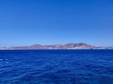 Nefes kesici ve çarpıcı bir okyanus manzarası berrak mavi gökyüzünün altında canlı bir mavi deniz ve kayalık adalar sergiliyor.