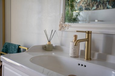 Altın musluk, mermer tezgah ve seramik leğen, sazlık yayıcı ve yumuşak ayna yansıtıcısı ile yakın çekim zarif lavabo, içerik yaratıcısı için biçimlendirilmiş