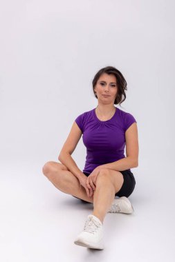 Stüdyoda oturmuş bir kadın dizini serinletiyor, gevşemiş ifade, yağmur sonrası gerilme, beyaz spor ayakkabılar, siyah şort, iyileşme rutini, dikkatli.