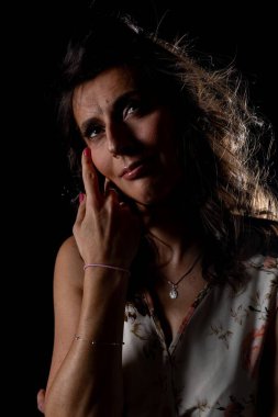 Boyalı beyaz bir kadın yanağa dokunuyor, loş bir stüdyo, çarpıcı bir ışık, parlak kırmızı boya ve teri vurguluyor, derin düşüncelere dalmış bir ifade, el yazısı.