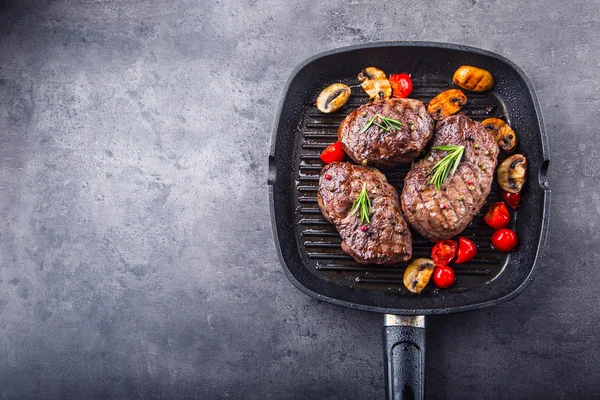 Bife grelhado. Porções de carne grossa bifes de lombo suculentos na grelha panela de teflon ou placa de madeira velha — Fotografia de Stock