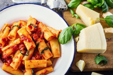 Pasta. Italian and Mediterrannean cuisine. Pasta Rigatoni with tomato sauce basil leaves garlic and parmesan cheese. An old home kitchen with old kitchen utensils clipart