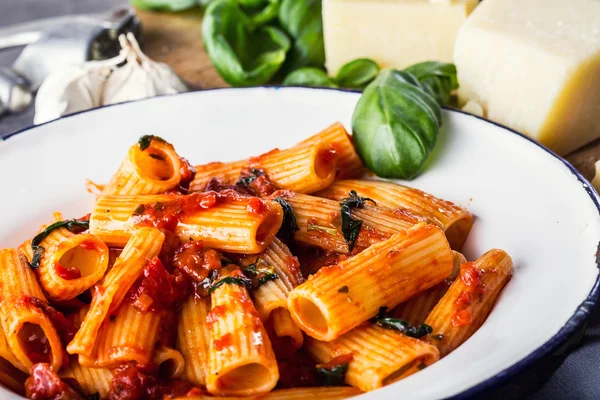 Pasta. Italian and Mediterrannean cuisine. Pasta Rigatoni with tomato sauce basil leaves garlic and parmesan cheese. An old home kitchen with old kitchen utensils — Stock Photo, Image