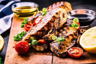 Çeri domatesli, mantarlı, otlu farklı çeşitlerde ızgara tavuk göğsü, ahşap bir tahtada limon kesimi veya teflon tavası. Geleneksel mutfak. Izgara mutfağı