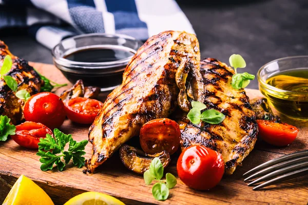 Grilled chicken breast in different variations with cherry tomatoes,  mushrooms, herbs, cut lemon on a wooden board or teflon pan. Traditional cuisine. Grill kitchen — Stock Photo, Image