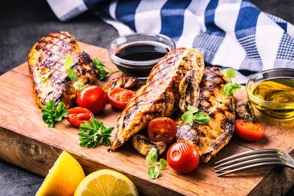 Grilled chicken breast in different variations with cherry tomatoes,  mushrooms, herbs, cut lemon on a wooden board or teflon pan. Traditional cuisine. Grill kitchen — Stock Photo, Image