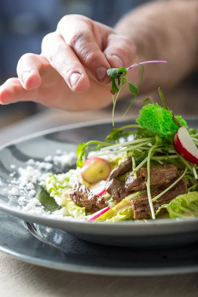 Chef en cocina de hotel o restaurante, solo manos. Está trabajando en la decoración de micro hierbas. Preparación de ensalada de verduras con trozos de carne de pollo a la parrilla - solomillo virgen —  Fotos de Stock