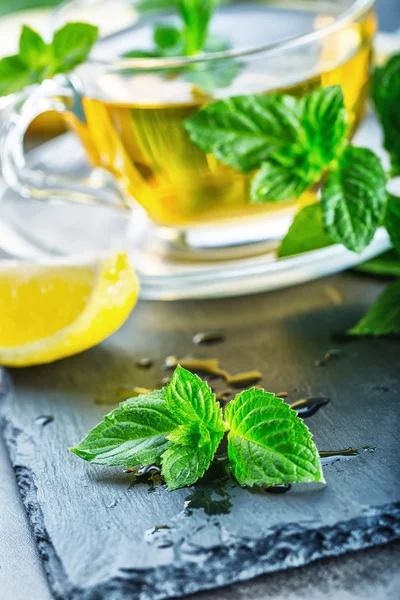 Hoja de menta. Hojas de menta. Té. Té de menta. Té de hierbas. Té en una taza de vidrio, hojas de menta, té seco, lima en rodajas. té de hierbas y hojas de menta en un plato de pizarra en un restaurante o salón de té —  Fotos de Stock