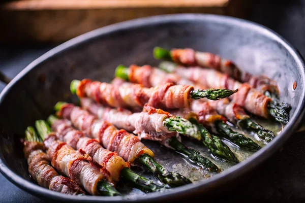 Sparris. Sparris och rulle bacon. Grillad sparris med rullad bacon och stekt ägg. Stekt gammal stekpanna full med rullad bacon med grön sparris och stekt ägg — Stockfoto