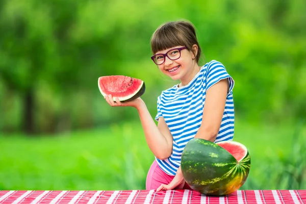 Ребёнок ест арбуз. Дети едят фрукты в саду. Девочка-подросток в саду держит кусок арбуза. счастливая девочка, которая ест арбуз. Девочка с газами и зубными скобками — стоковое фото