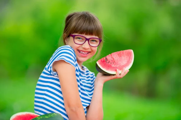 Niño comiendo sandía. Los niños comen frutas en el jardín. Pre adolescente en el jardín sosteniendo una rebanada de sandía. niña feliz comiendo sandía. Niña con gases y aparatos ortopédicos — Foto de Stock