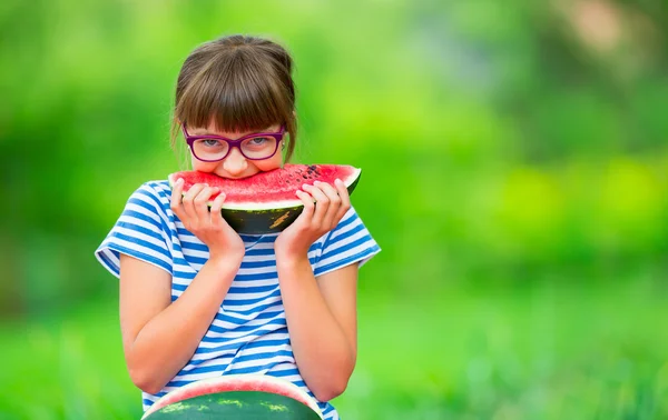 Ребёнок ест арбуз. Дети едят фрукты в саду. Девочка-подросток в саду держит кусок арбуза. счастливая девочка, которая ест арбуз. Девочка с газами и зубными скобками — стоковое фото