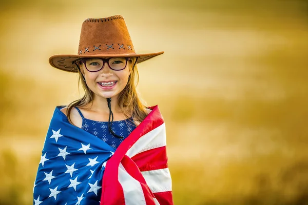 Bella giovane ragazza pre-adolescente con un cappello da cowboy americano nel campo di mais e la bandiera americana — Foto Stock