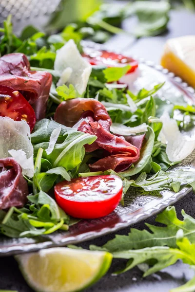Gedroogd rundvlees bresaola. Salade bresaola rucola baby spinazie tomaten limoen en Parmezaanse kaas — Stockfoto