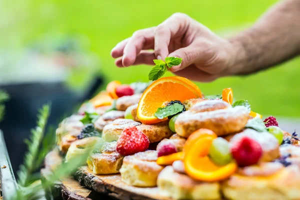 Chef prepares a plate of cakes with fresh fruits. He is working on the herb decoration. Outdoor garden party — Stock Photo, Image