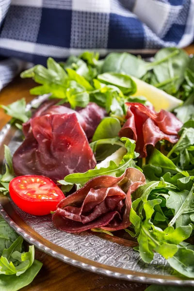 Gedroogd rundvlees bresaola. Salade bresaola rucola baby spinazie tomaten limoen en Parmezaanse kaas — Stockfoto