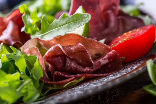 Dried beef bresaola. Salad bresaola arugula baby spinach tomatoes lime and cheese parmesan — Stock Photo, Image