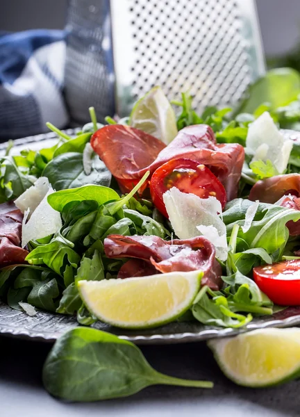 Dried beef bresaola. Salad bresaola arugula baby spinach tomatoes lime and cheese parmesan — Stock Photo, Image