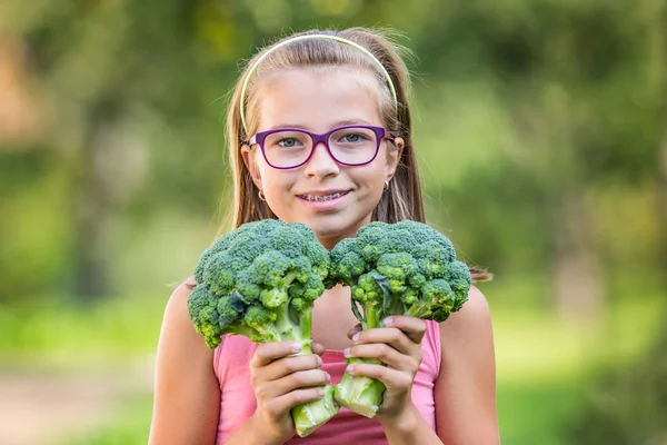 Engraçado bonito menina segurando em mãos repolho vermelho e brócolis. Fundo borrado no jardim. Menina pré-adolescente com óculos e aparelho de dentes — Fotografia de Stock