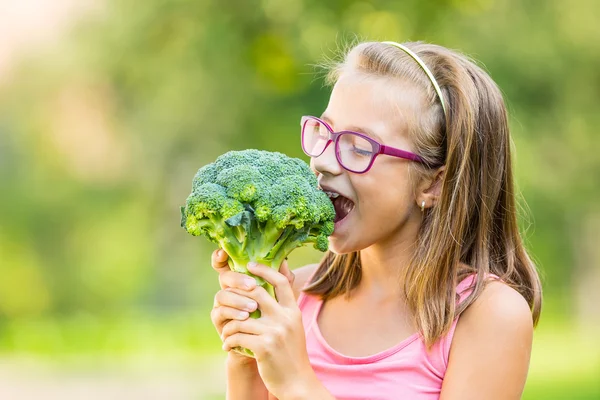 Chica linda divertida sosteniendo en las manos la col roja y el brócoli. Fondo borroso en el jardín. Pre-adolescente joven con gafas y aparatos ortopédicos — Foto de Stock