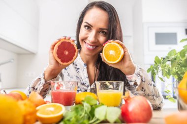 Kadının elinde kırmızı ve sarı ellerinde turuncu ve önünde taze meyve suları var..
