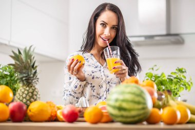 Kız, taze sıkılmış portakal suyunu etrafını meyve çeşitleriyle sarmış kağıt kamışla yudumluyor..