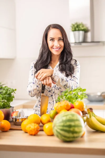 微笑的女孩在厨房里拿着一把小刀 周围都是新鲜的水果和香草 — 图库照片