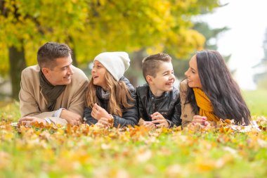 Mutlu bir aile, sonbaharda aileleri çocuklarıyla konuşurken battaniyenin üzerinde sohbet ediyor..