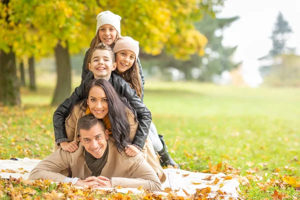 Çocuklu bir aile, bir sonbahar günü doğada insan piramidi yapmak için battaniyeye uzanır..