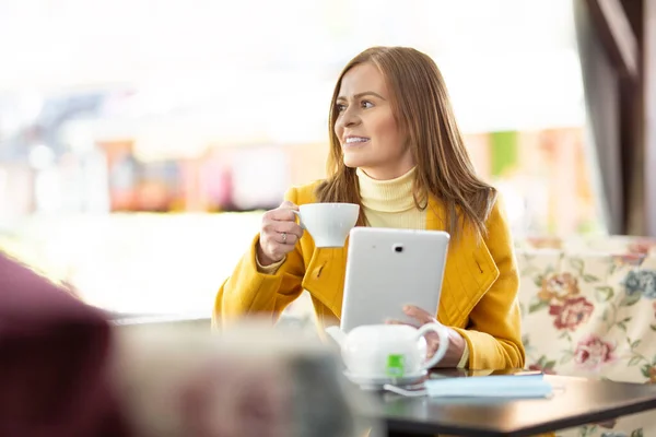 タートルネックを身に着けている女性は カフェでタブレットを保持茶のカップを飲みます — ストック写真