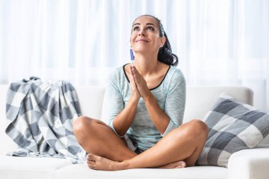 Kanepede bacak bacak bacak üstüne atmış bir kadın hamilelik testi için dua ediyor..