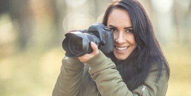 Güzel gülümseyen esmer fotoğrafçı sonbahar havasında fotoğraf çekiyor..