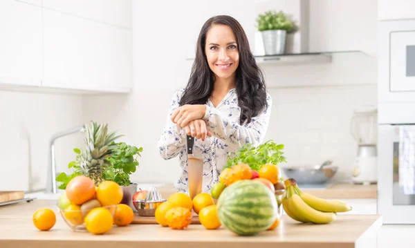 Uśmiechnięta Młoda Kobieta Trzyma Nóż Kuchni Otoczony Świeżymi Owocami Ziołami — Zdjęcie stockowe