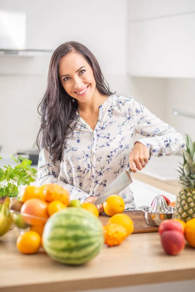 Sorridente Giovane Donna Affettare Frutta Arancione Cucina Circondata Frutta Fresca — Foto Stock