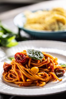 Kırmızı soslu spagetti, domates ve fesleğen tabakta servis edilir..