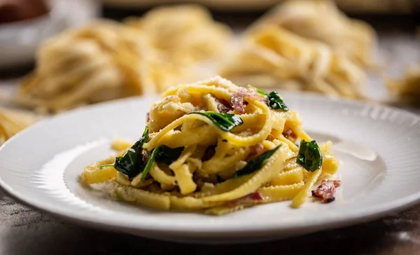Cooked fresh fettuccine pasta served on a plate with spinach and bacon.