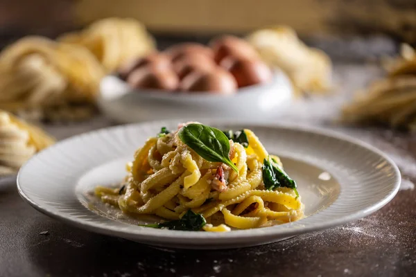 Cooked fresh fettuccine pasta served on a plate with spinach and bacon.