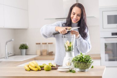 Evde süveter giyen bir kadın tarafından miksere muz kesilerek meyve püresi hazırlama.