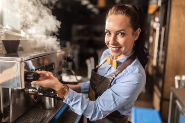 Profesyonel, iyi giyimli bayan barista bir kafede kahve makinesinden buhar çıkartıyor..
