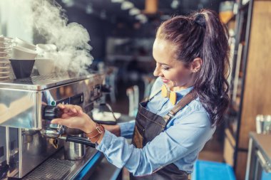 Profesyonel, iyi giyimli bayan barista bir kafede kahve makinesinden buhar çıkartıyor..