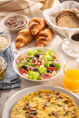 Omlet, kruvasan, salata, ekmek, yulaf ezmesi, reçel, waffle, bal, çukulata, kahve ve portakal suyu da dahil olmak üzere çeşitli yiyecekler..