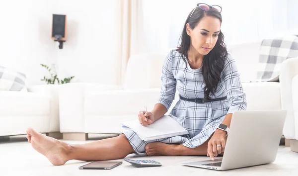 Home office working woman takes notes and writes on notebook while sitting on living room floor.