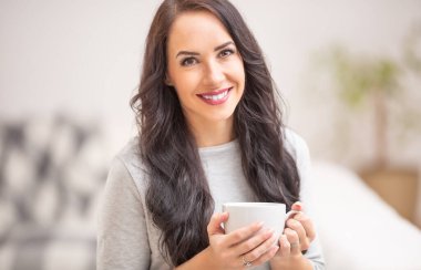 Genç esmer kadın elinde bir fincan çay ya da kahve tutuyor ve güzel bir koku yayıyor..