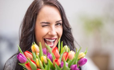 Ulusal Kadınlar Günü 'nde göz kırpan ve elinde lale dolu bir buket tutan mutlu siyah saçlı kadın..