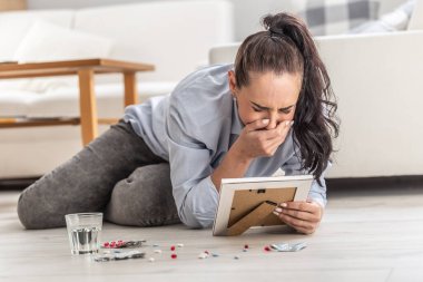Woman considering drug overdose suicide crying over a picture of someone she loved and lost.