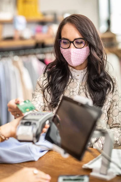 Woman worrying about coronavirus pays contactless by a card in the store wearing a face mask.