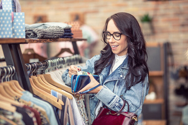 Woman happy about the content in her wallet selects clothes to buy in the clothes store.