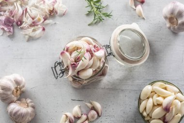 Sarımsak karanfilleriyle dolu bir kavanoz, soyulmuş sarımsak karanfilleri ve baharatlı biberiyelerle dolu bir kase..