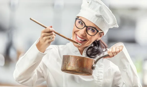穿着职业装的女厨师微笑着 用装铜壶的木勺品尝食物 — 图库照片